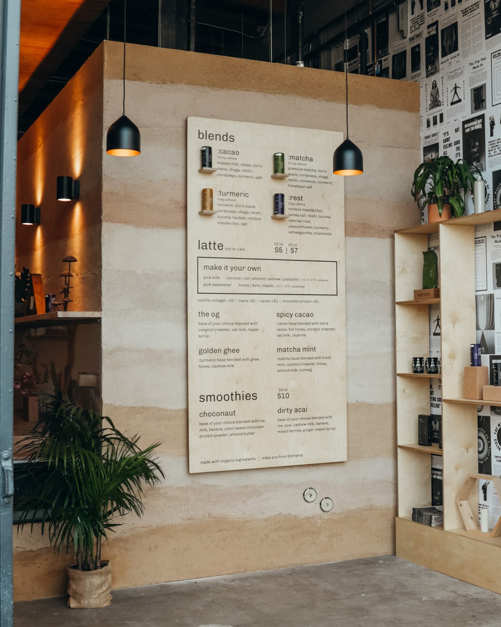 Menu board mounted on the Rammed Earth bar at MUD\WTR Gather beside plywood shelving and a potted palm.