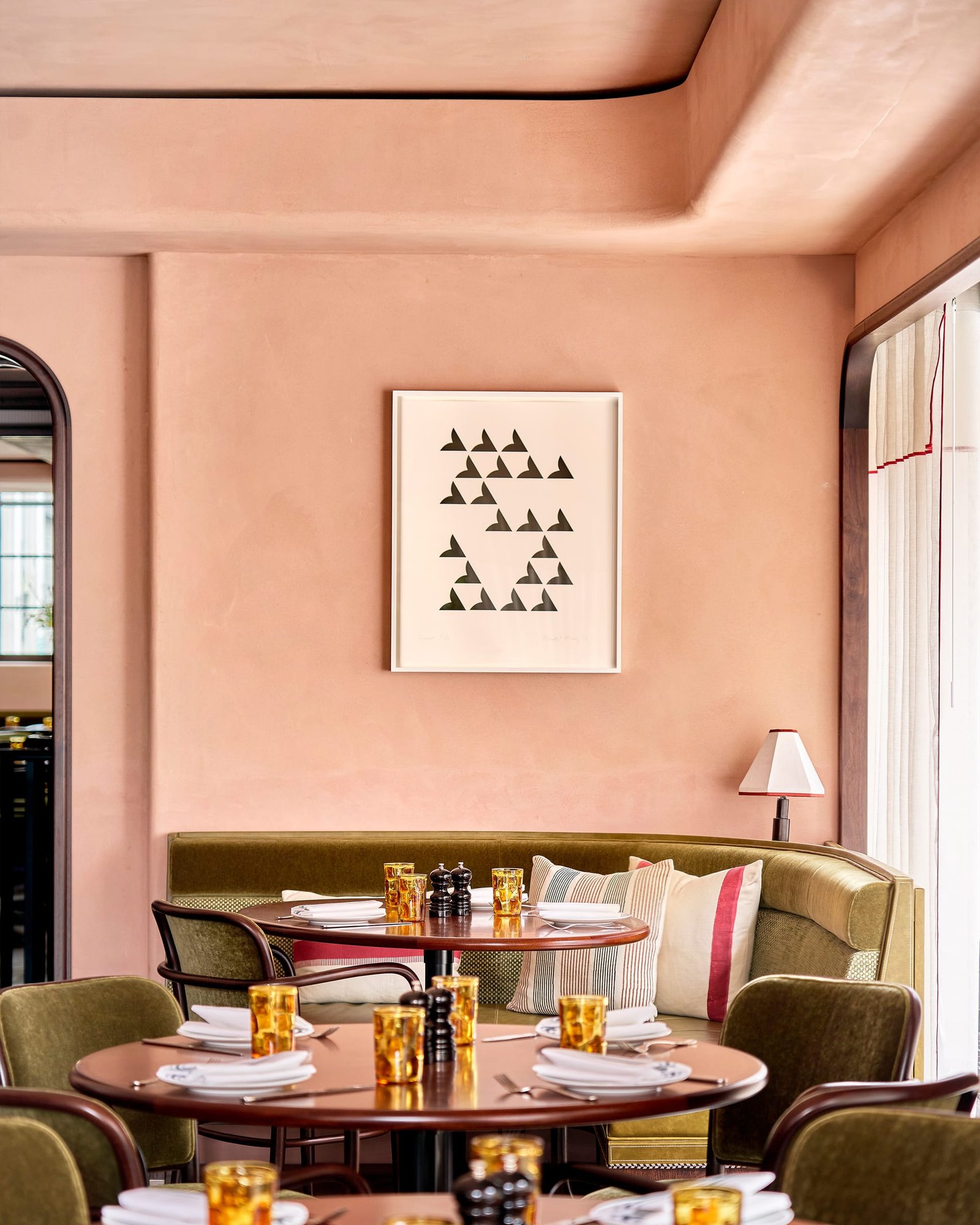 Nipotina corner with a framed print on smooth nude clay plaster above a round table and olive banquette.