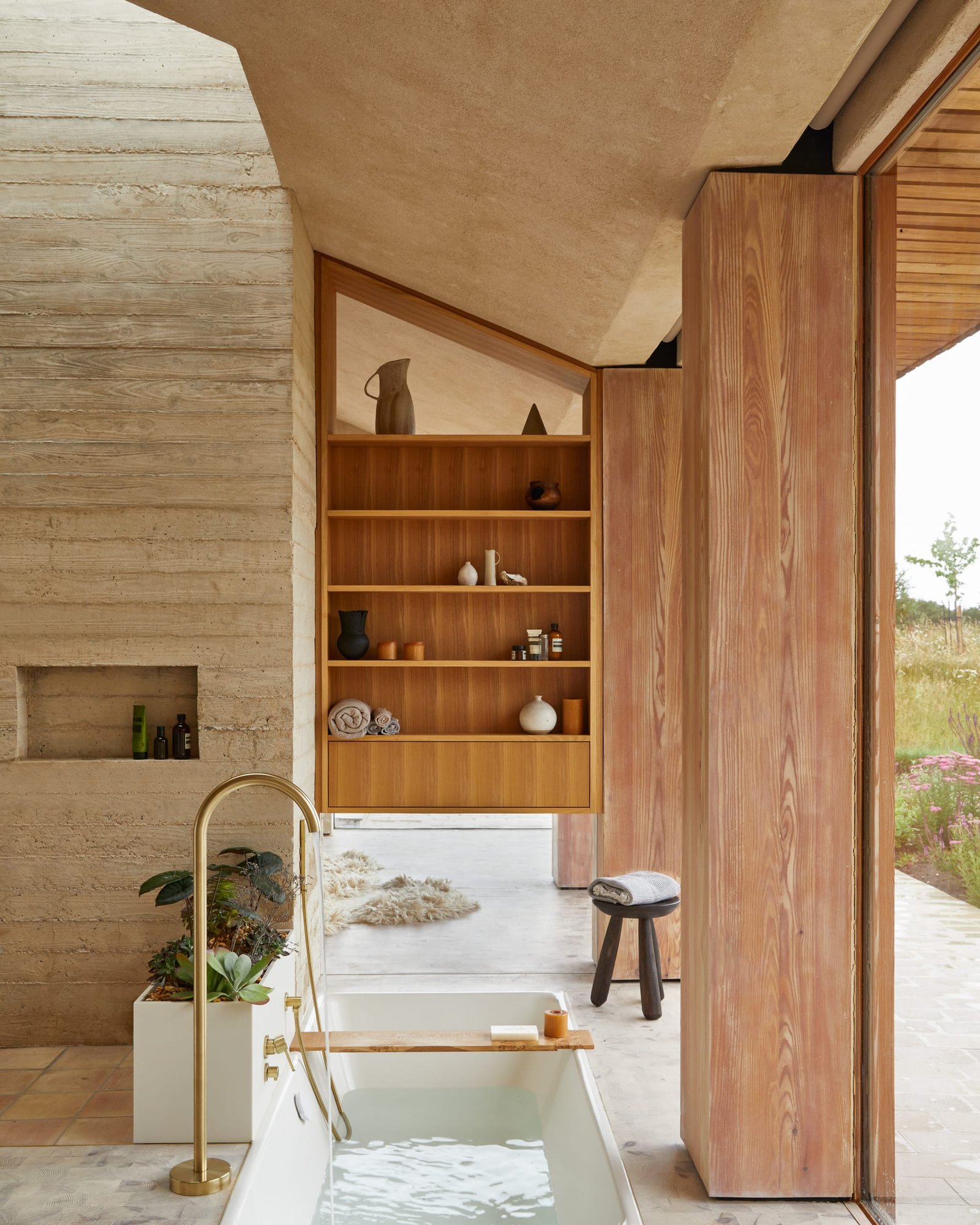 Sunken bath at The Makers Barn beneath a clay-plastered vaulted ceiling, brass tap and shuttered concrete wall.