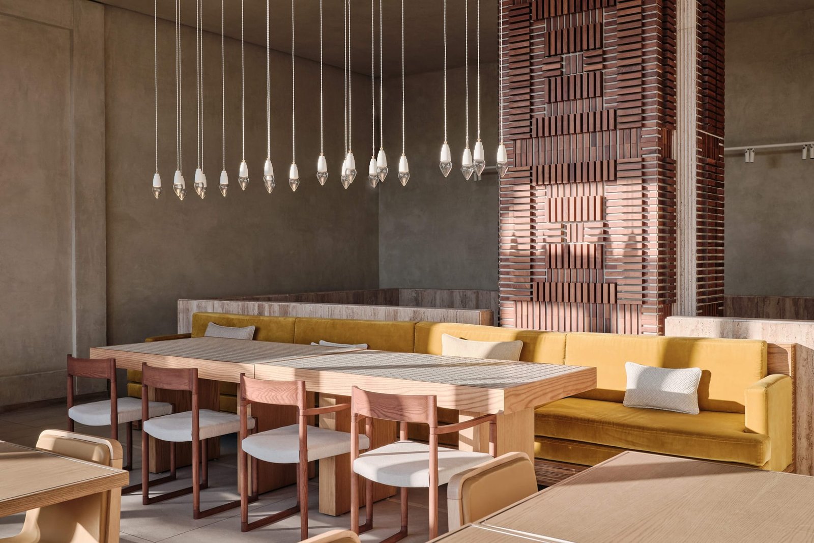 Toplum dining room with mustard banquettes, a brick-clad column and a row of pendant bulbs against clay plaster.