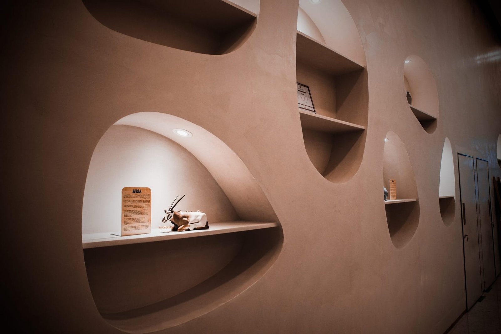 Curved blush-taupe Microtadelakt lime plaster display wall with organic oval niches at Afraa Boutique, Lusail