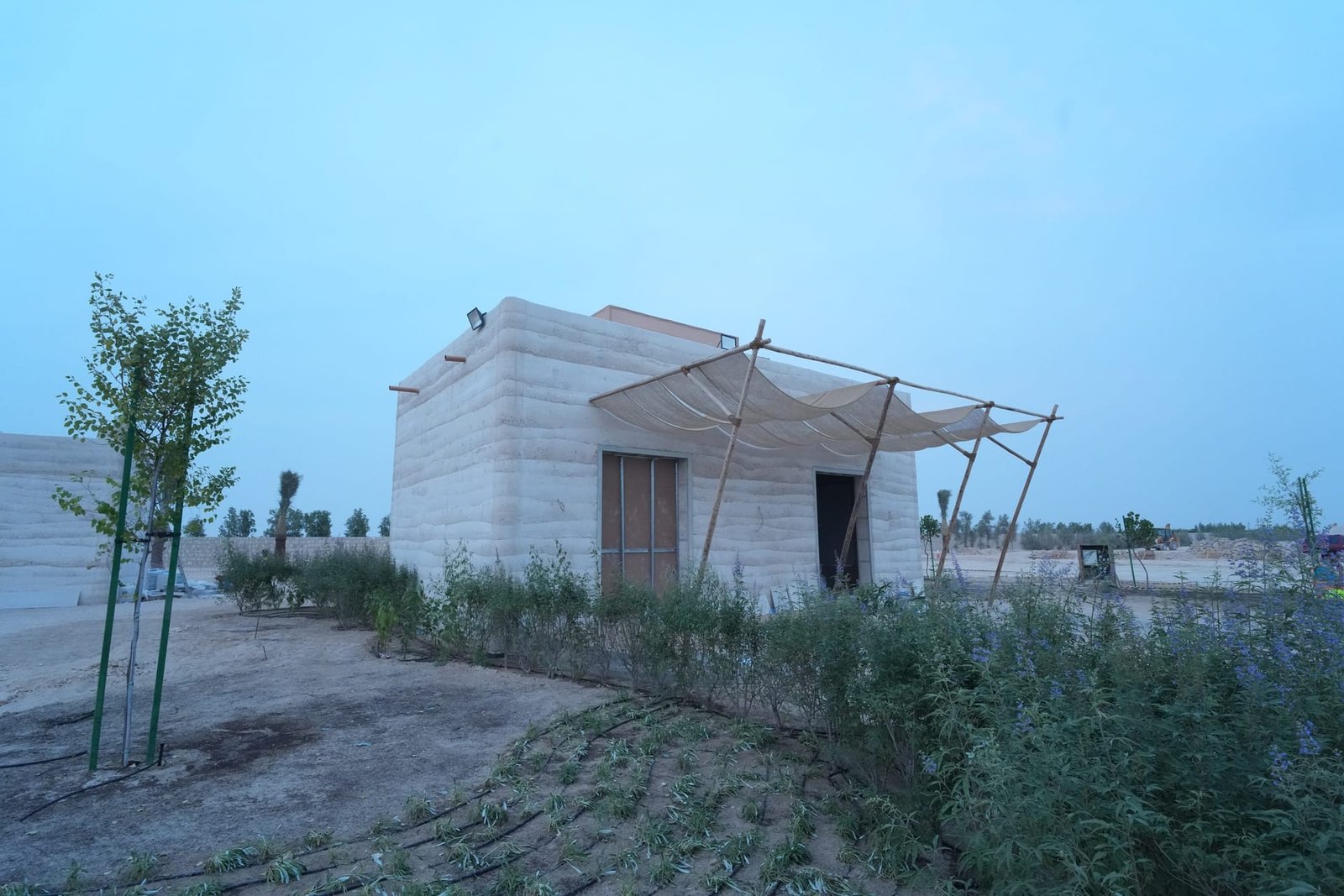 Layered strata walls of an in-situ rammed earth guest building at dusk, Al Kaaban Resort, Qatar