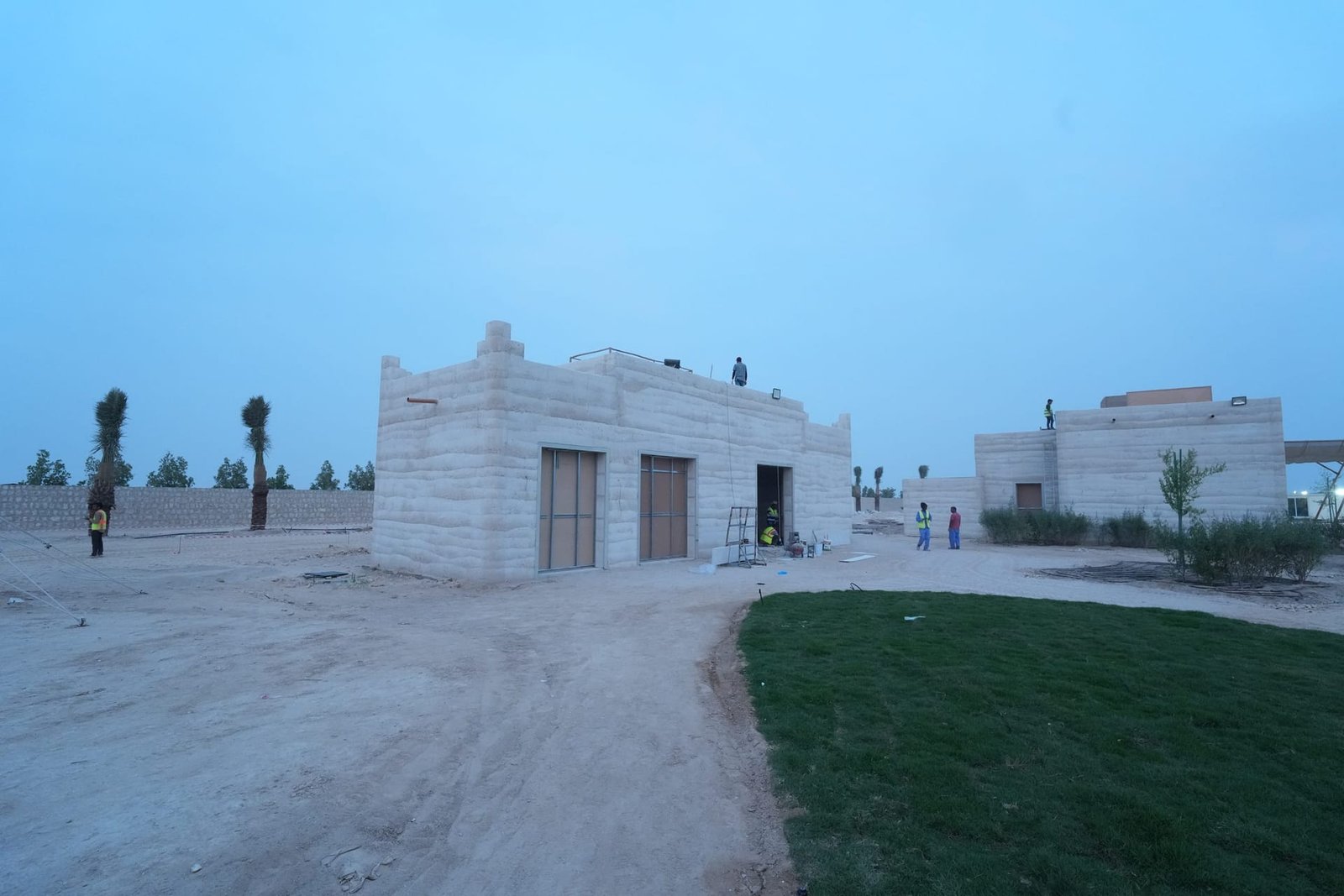 Two rammed earth buildings with stepped parapets under construction, crews working on the strata walls