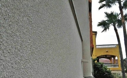 Pale grey projected cork wall in raking light with palms and an ochre building beyond
