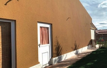 Ochre projected cork facade on a single-storey house with a white door