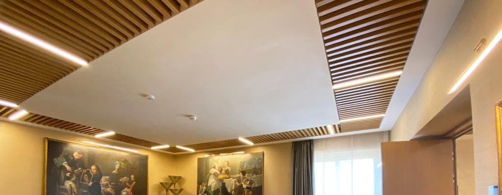 Seamless acoustic plaster ceiling panel framed by timber slats in a meeting room at Banca d’Italia, Rome.