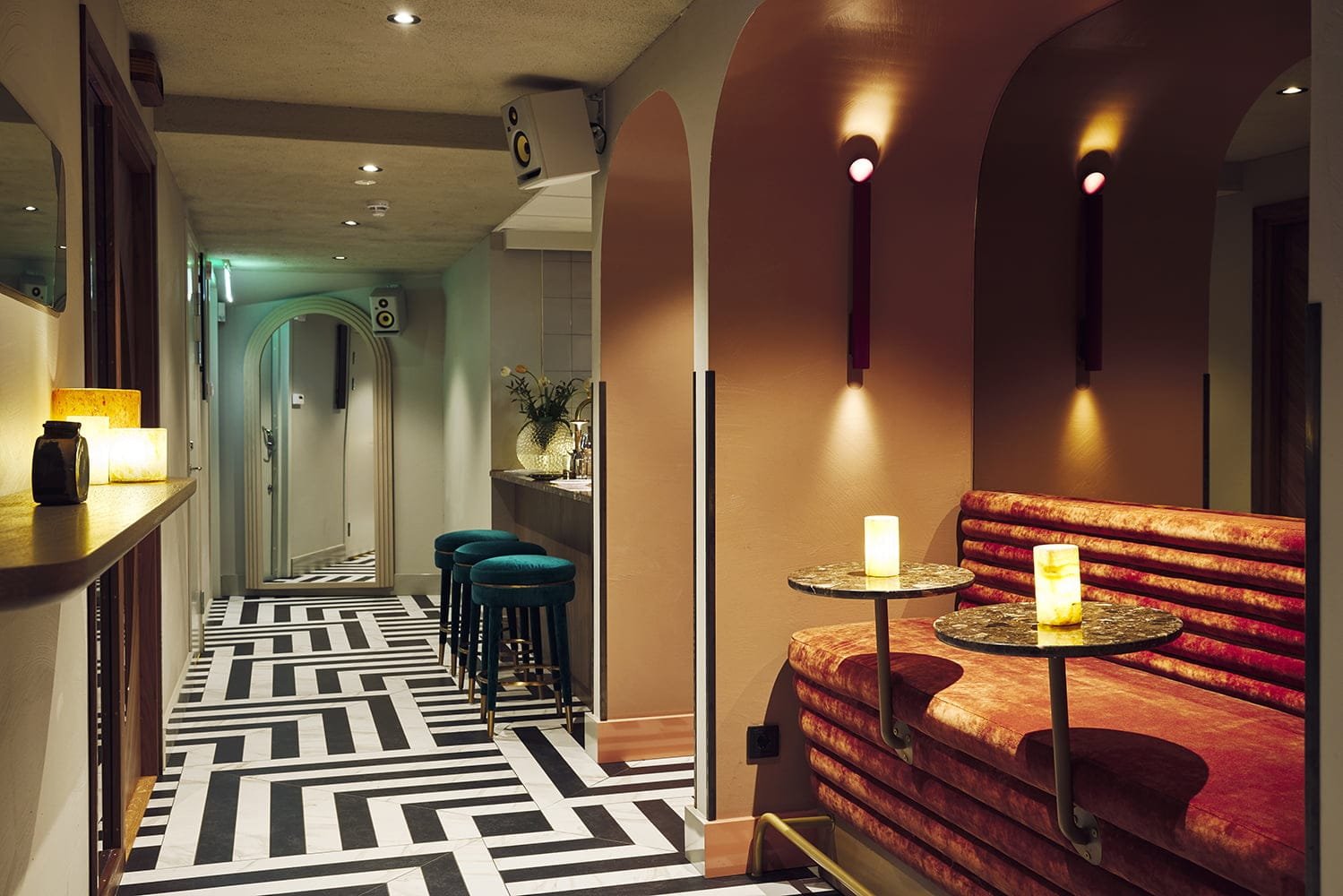 Arched booths with velvet banquettes and teal stools off a corridor at Melody Club, London, under a plastered arched ceiling
