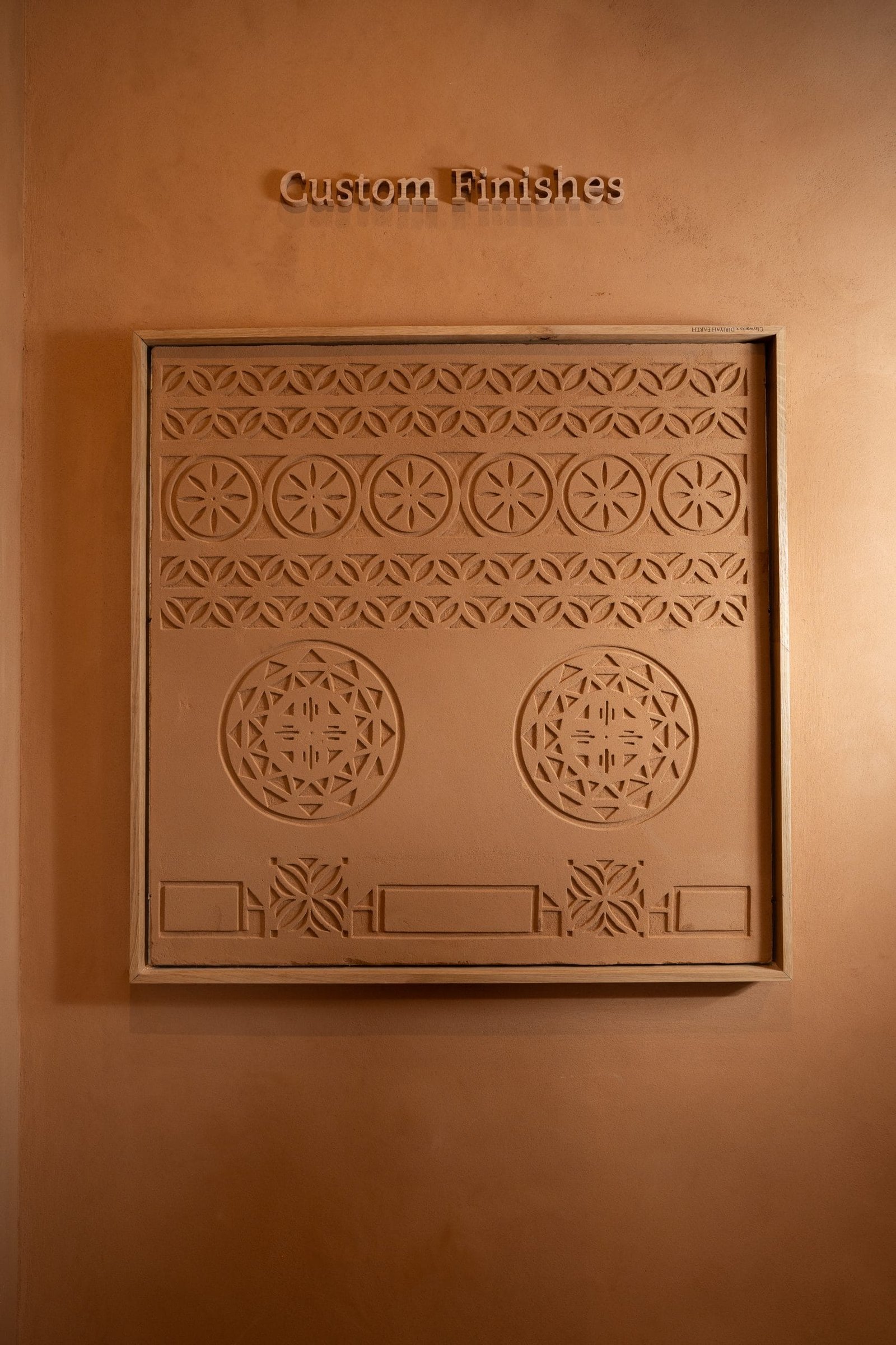 The Custom Finishes carved clay plaster relief at the Conmarble showroom, seen square on in warm downlight.