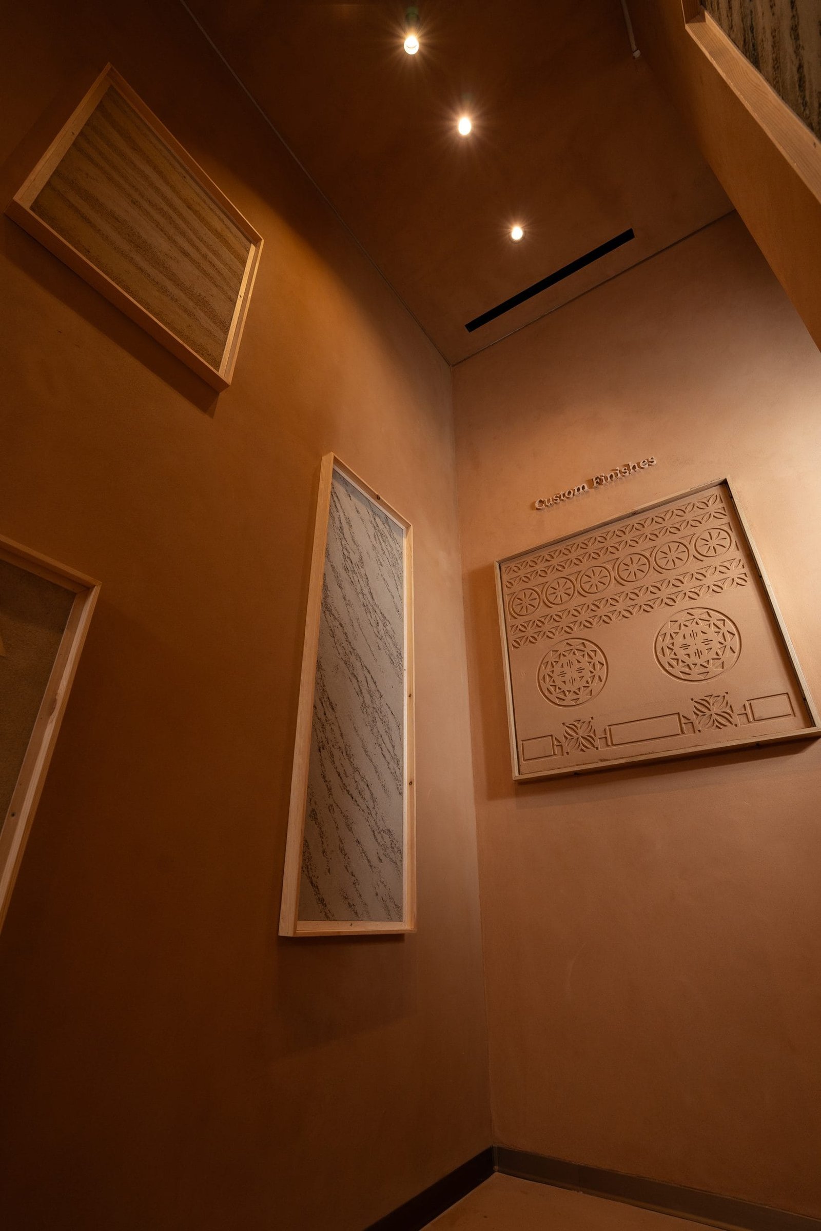 Framed clay plaster panels on terracotta walls, Custom Finishes gallery, Riyadh showroom