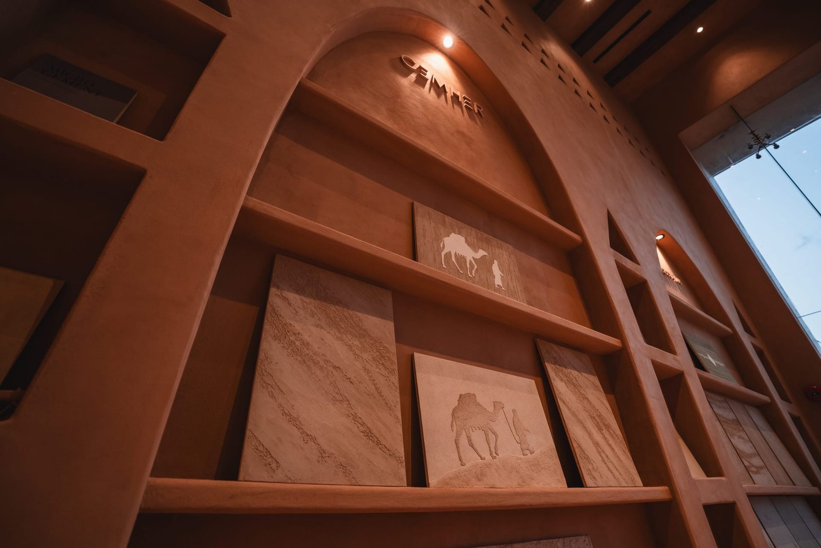 Cemher arch at the Conmarble showroom holding sand-toned microcement panels carved with camel and dune motifs.