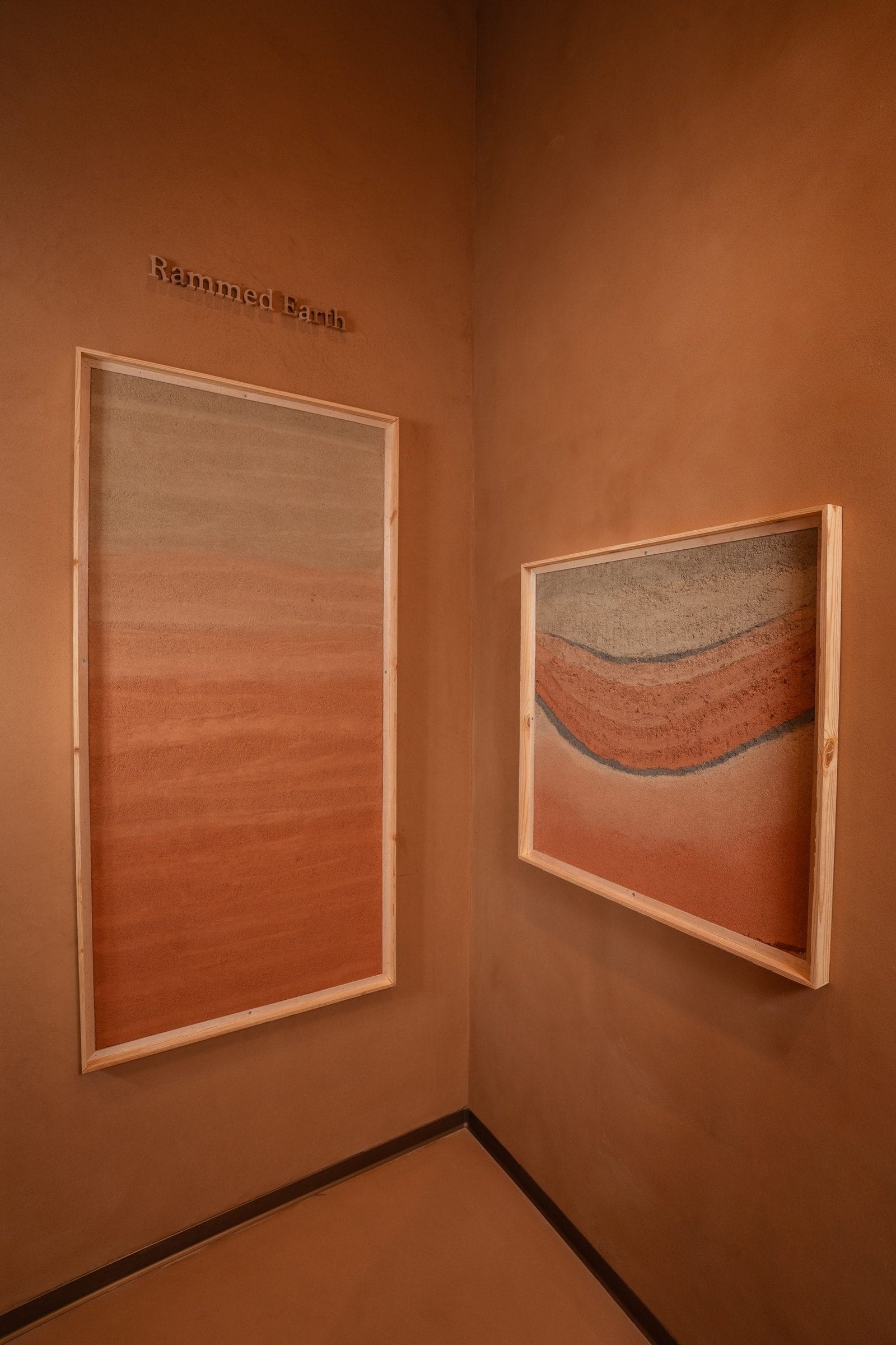 Framed rammed earth plaster panels stepped along a clay-plastered wall, Riyadh showroom
