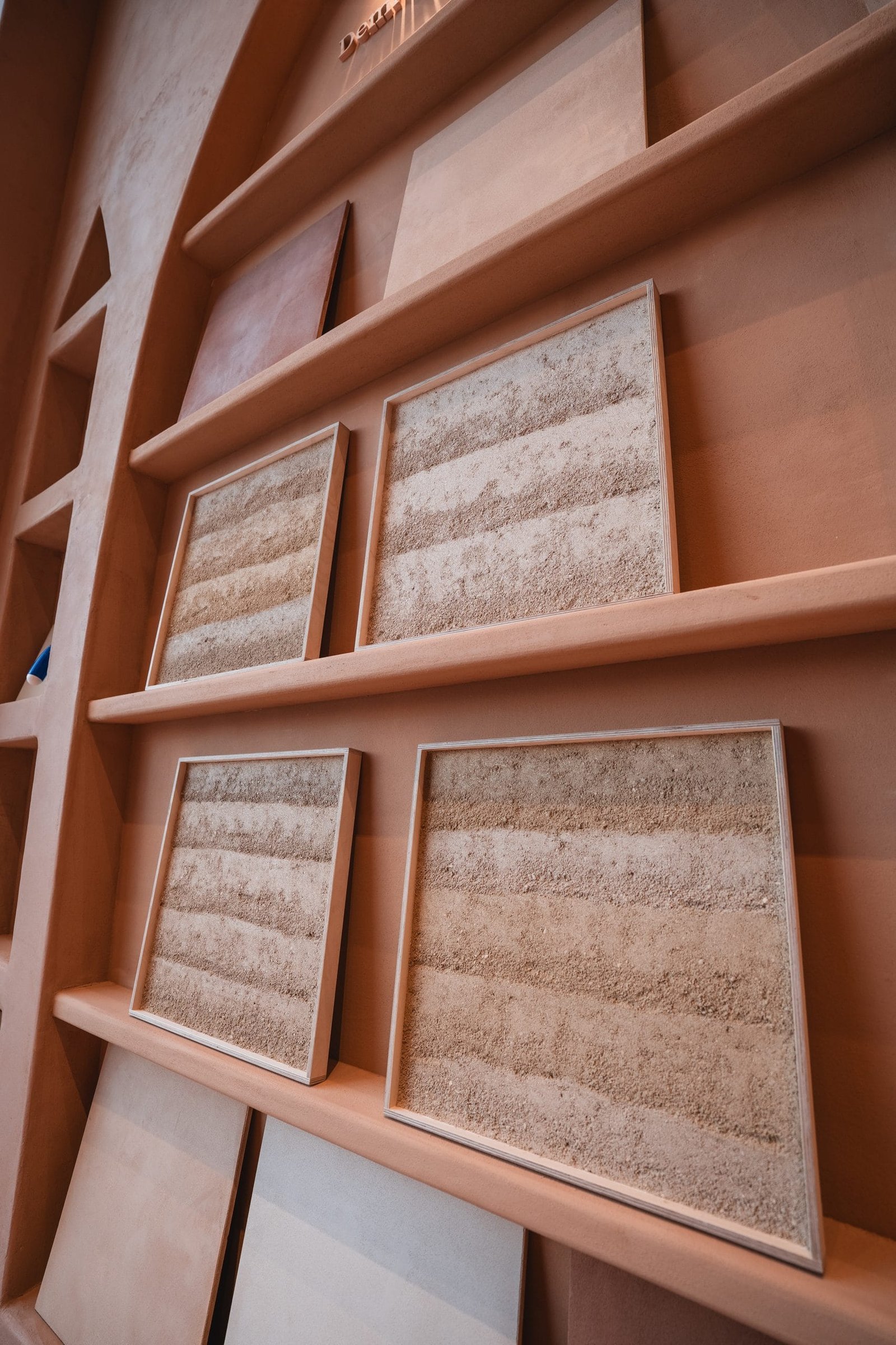 Four framed Rammed Earth Finish samples, pale sand bands with open grain, Riyadh showroom