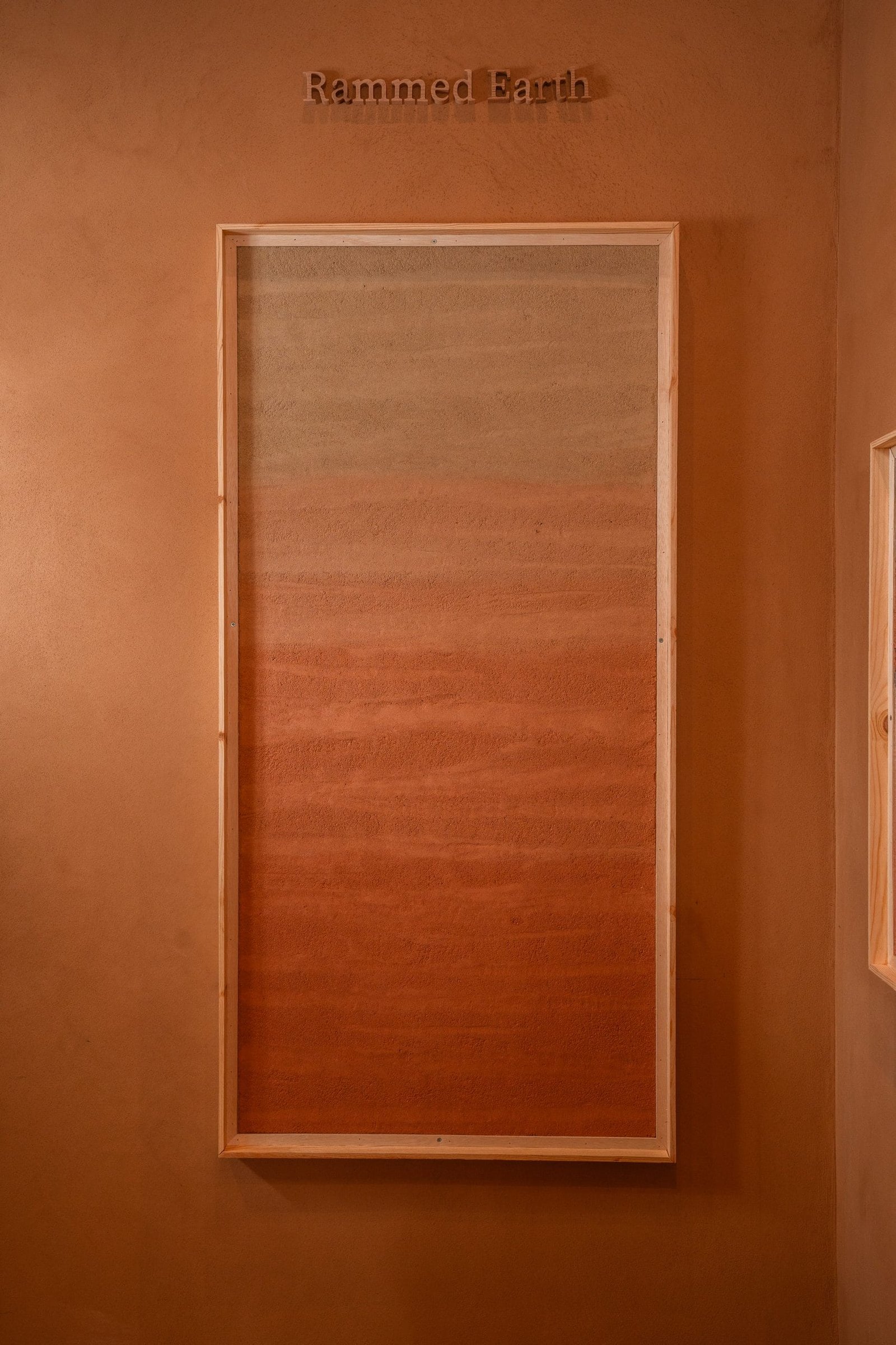 Framed rammed earth plaster panel graded grey through ochre to terracotta, Riyadh showroom